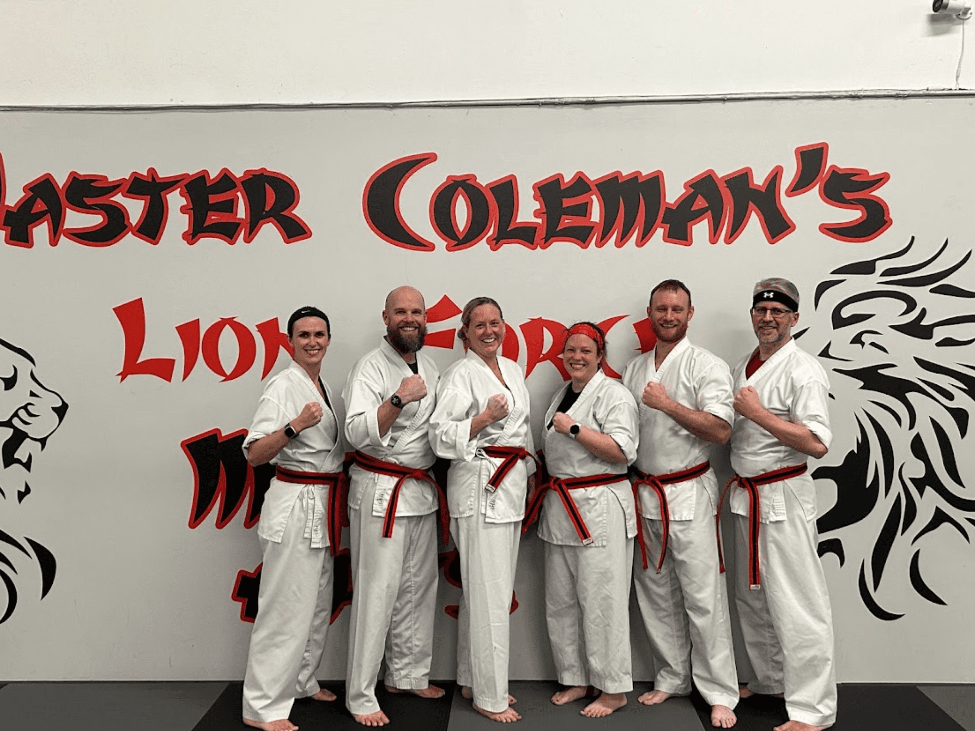 Group of six people, all wearing white martial arts uniforms, standing together in a room